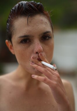 Short red-haired girl with freckles smokes after getting wet