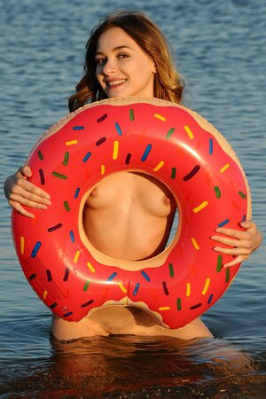 Slim teen model poses naked on the local beach with swim ring in the hands
