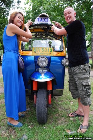 Hot female from Thailand poses in her slinky blue dress by a small taxi