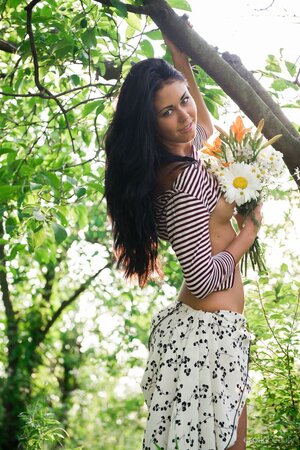 Raven-haired hussy with a bunch of flowers demonstrates her pussy in the woods