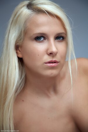 Long-haired blonde demonstrates medium boobs and shaved pussy in the studio