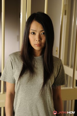 Oriental inmate girl demonstrates small breasts by the bars of the cell