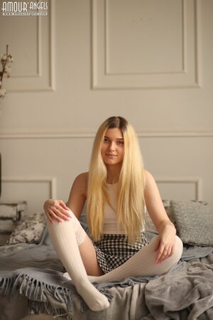 Young blonde beauty Suna undresses on top of her bed